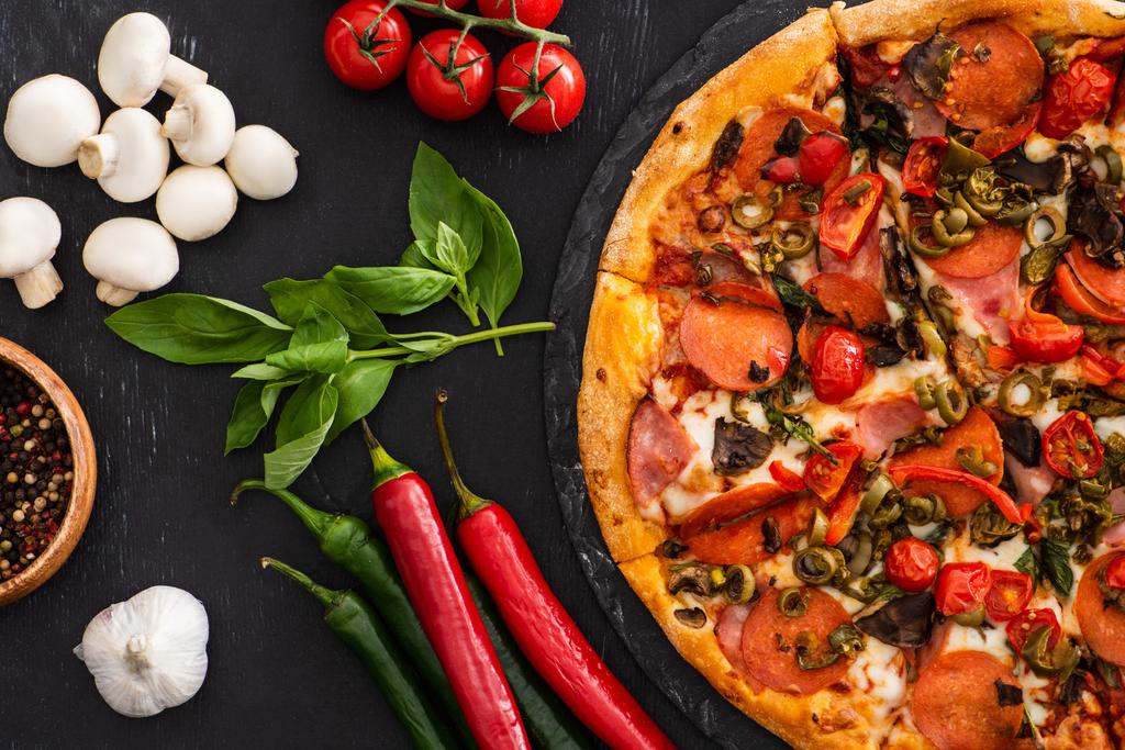 top view of delicious Italian pizza with vegetables and salami on black background - Photo, Image