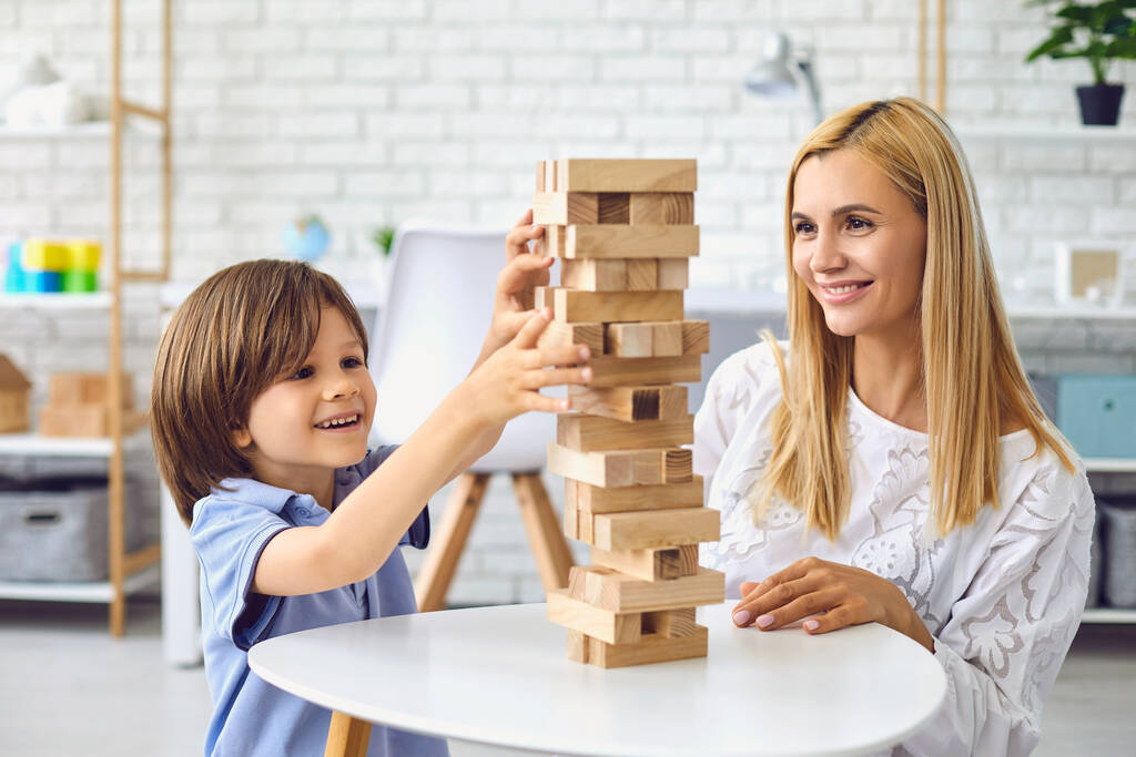 Menino edifício torre de blocos de madeira com a mãe em casa. Pais e criança jogando jogo de tabuleiro juntos dentro de casa
 - Foto, Imagem