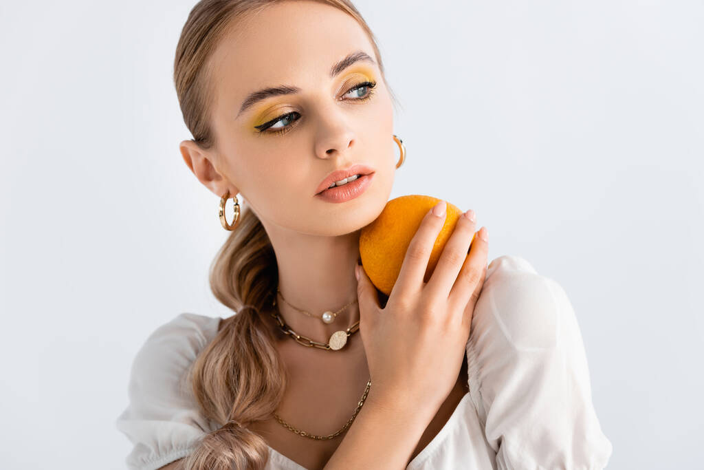 элегантная блондинка позирует с оранжевым и глядя в сторону изолированы на белом - Фото, изображение