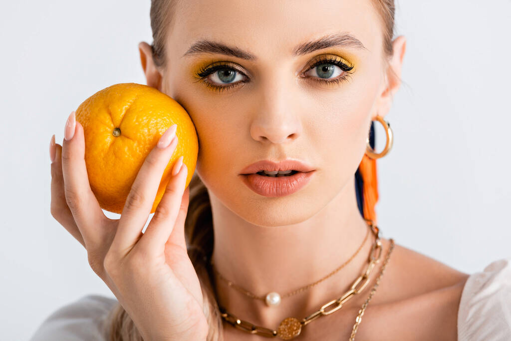 elegante mujer rubia sosteniendo naranja cerca de la cara aislada en blanco - Foto, Imagen