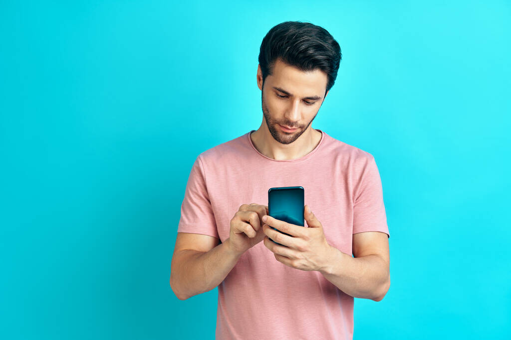 Bello uomo sorridente utilizzando smart phone su sfondo blu studio - Foto, immagini