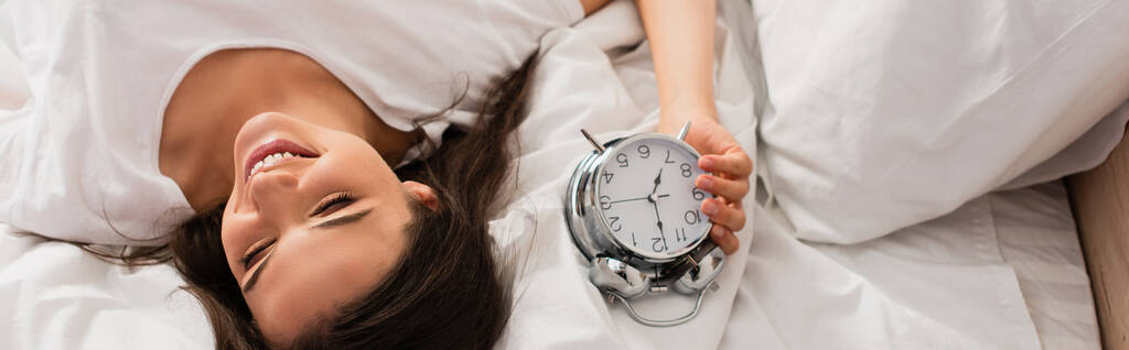 plano panorámico de mujer joven acostada en la cama con reloj despertador retro  - Foto, Imagen