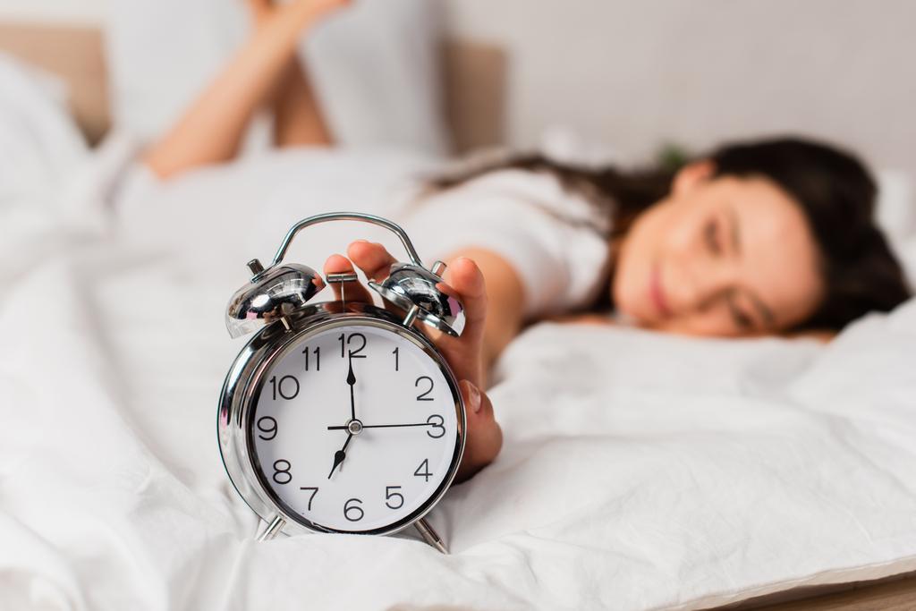 selective focus of woman lying on bed and reaching retro alarm clock  - Photo, Image