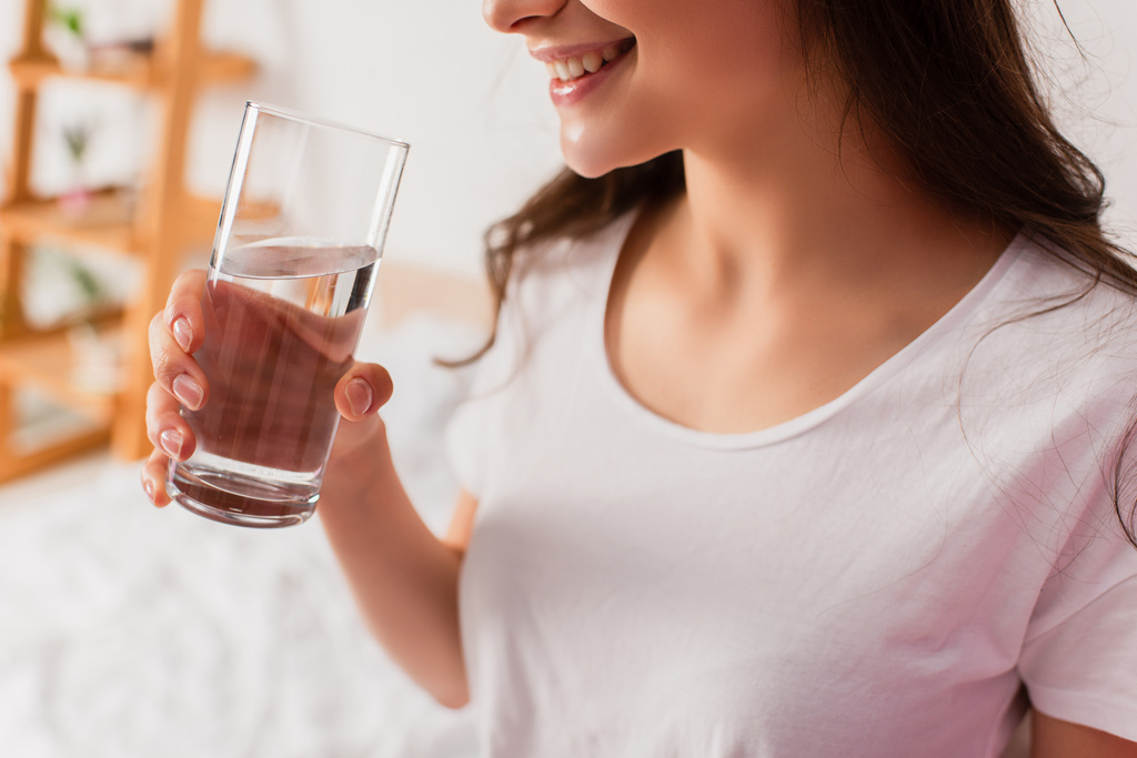 bijgesneden uitzicht op jonge brunette vrouw holding glas water - Foto, afbeelding