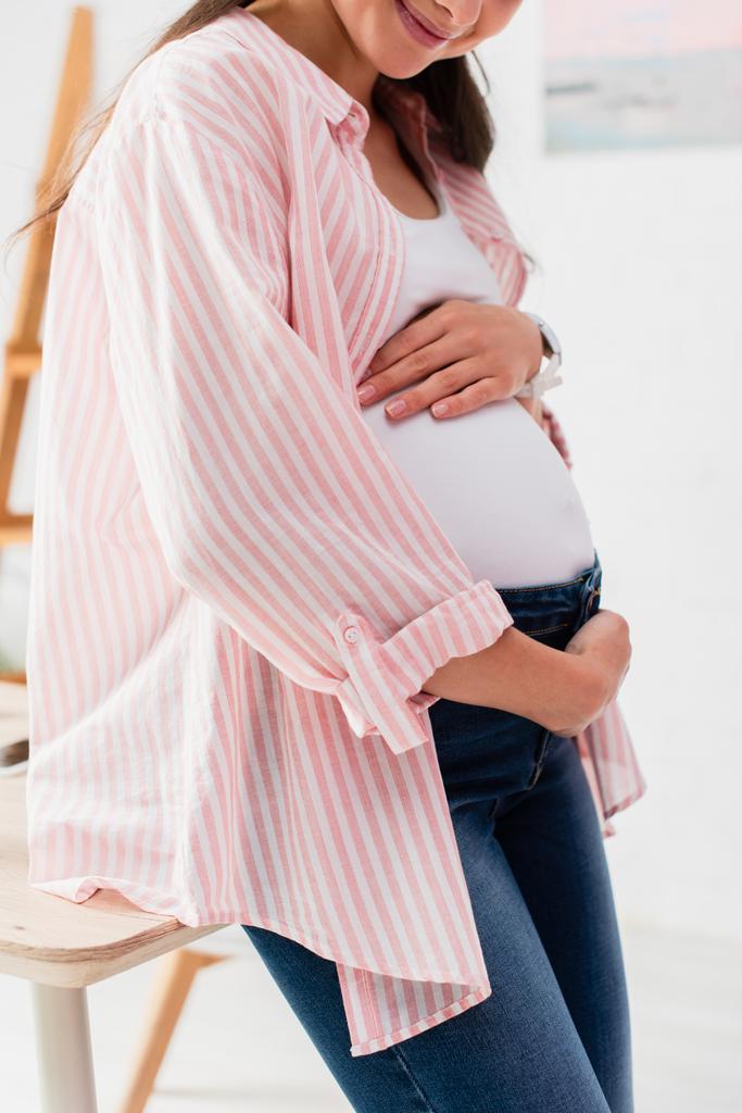 abgeschnittene Ansicht einer schwangeren Frau, die ihren Bauch zu Hause berührt  - Foto, Bild