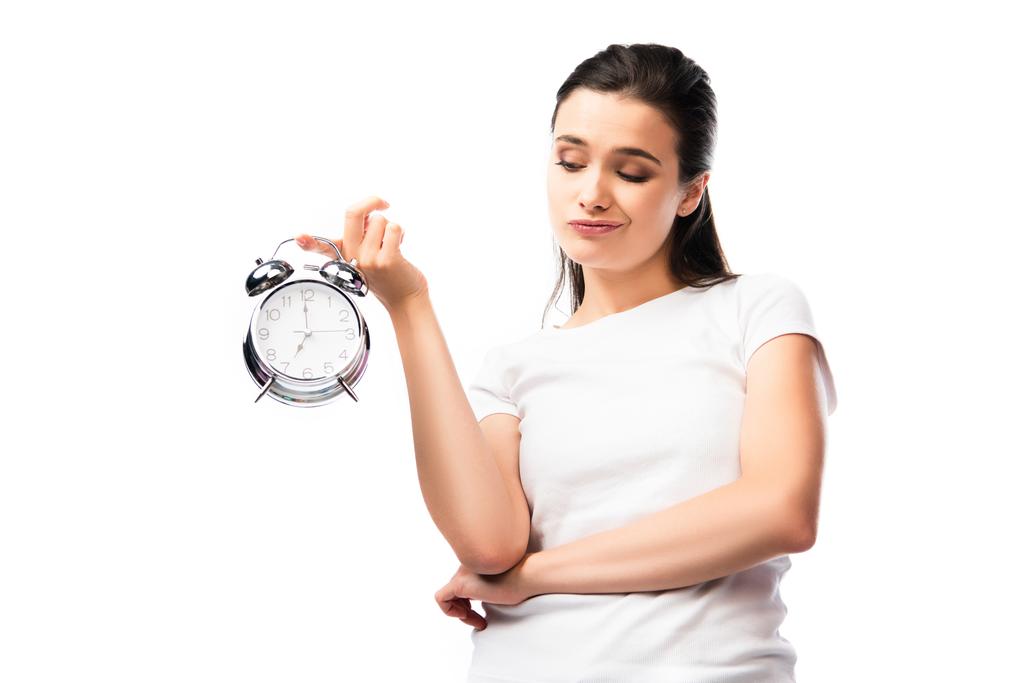 mujer insatisfecha en camiseta blanca mirando el reloj despertador retro aislado en blanco - Foto, Imagen