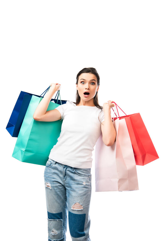 mulher chocada segurando sacos de compras e olhando para a câmera isolada no branco  - Foto, Imagem