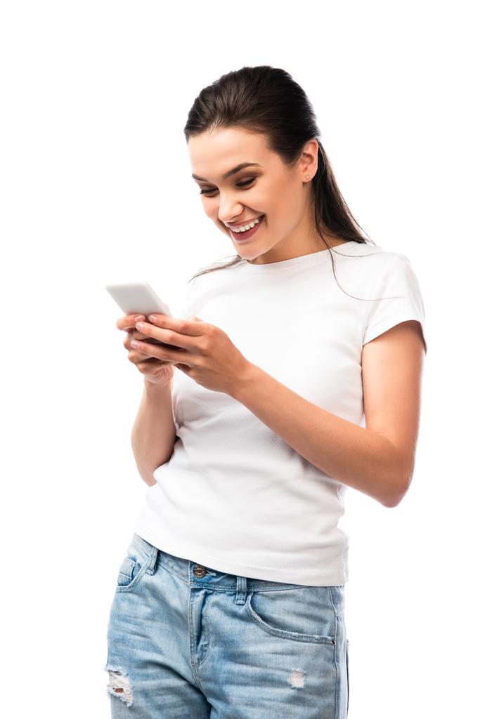 брюнетка женщина в белой футболке с помощью смартфона изолированы на белом - Фото, изображение