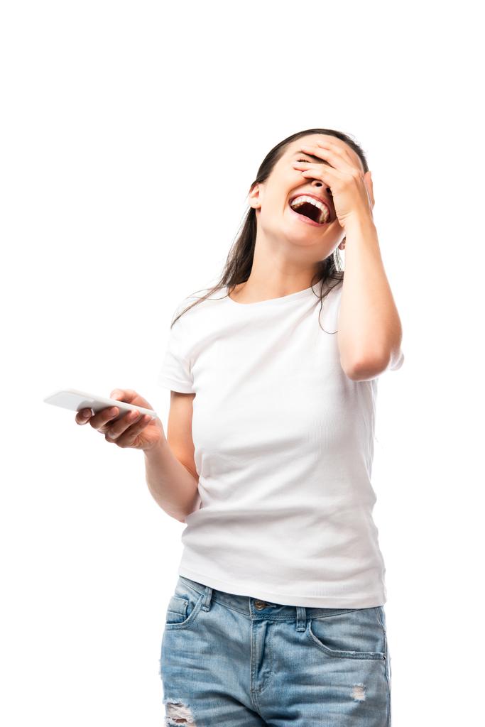 молода жінка прикриває обличчя, сміється і тримає смартфон ізольовано на білому
  - Фото, зображення