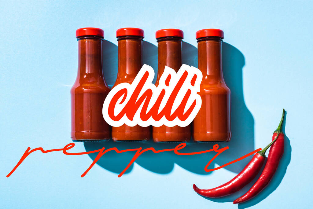 Vista dall'alto di peperoncino lettering vicino salsa di pomodoro in bottiglie su sfondo blu - Foto, immagini
