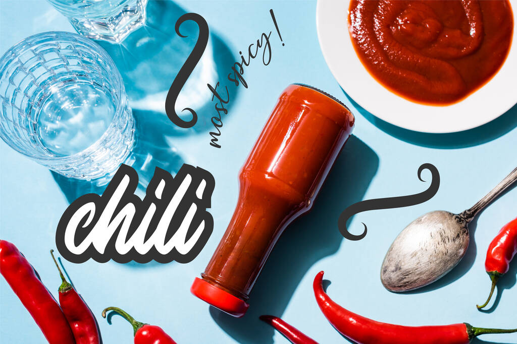 Bovenaanzicht van glazen met water, tomatensaus op bord en fles naast chili pepers bij meest pittige belettering op blauw  - Foto, afbeelding