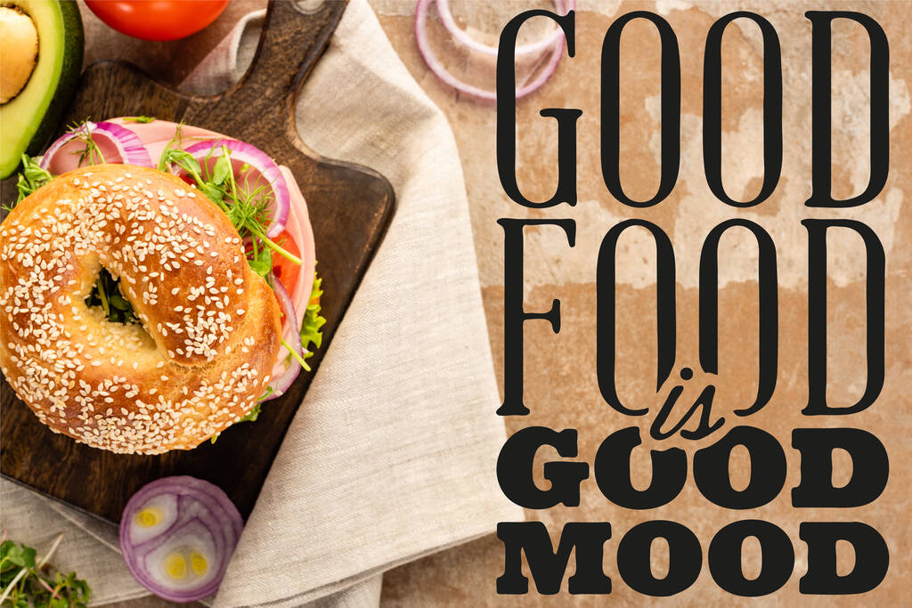 top view of bagel on wooden cutting board and cloth napkin near good food is good mood lettering on textured background - Photo, Image