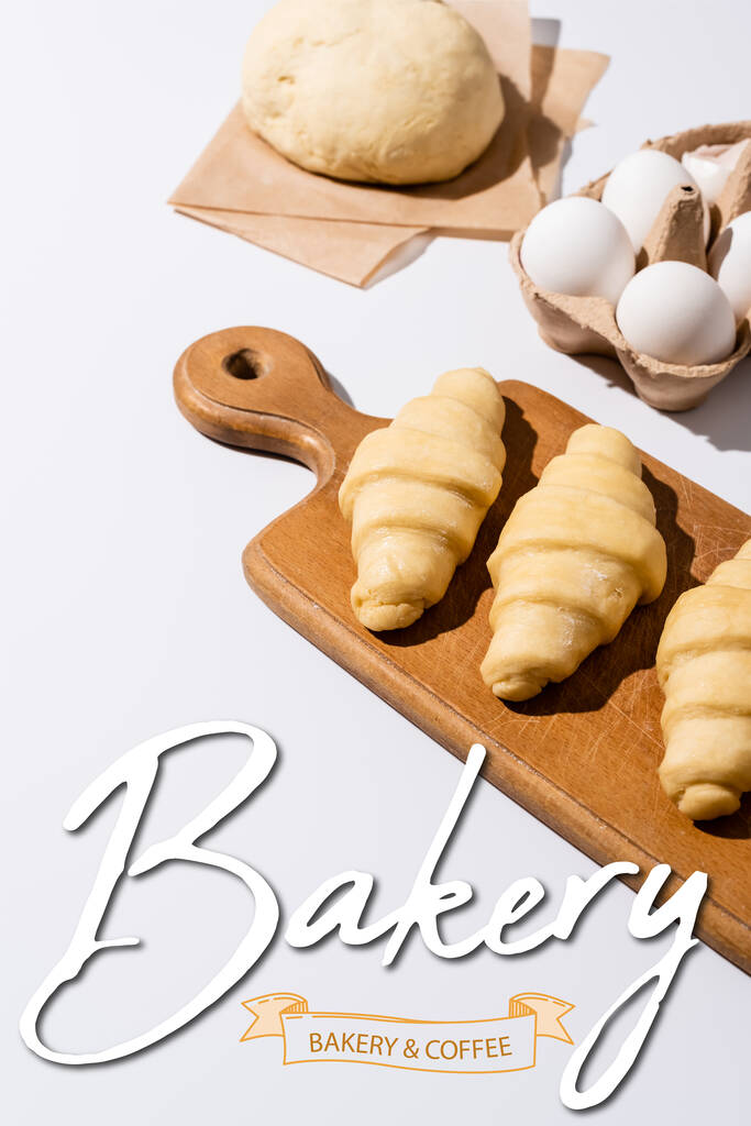 raw croissants on wooden cutting board near eggs, dough, bakery and coffee lettering on white  - Photo, Image