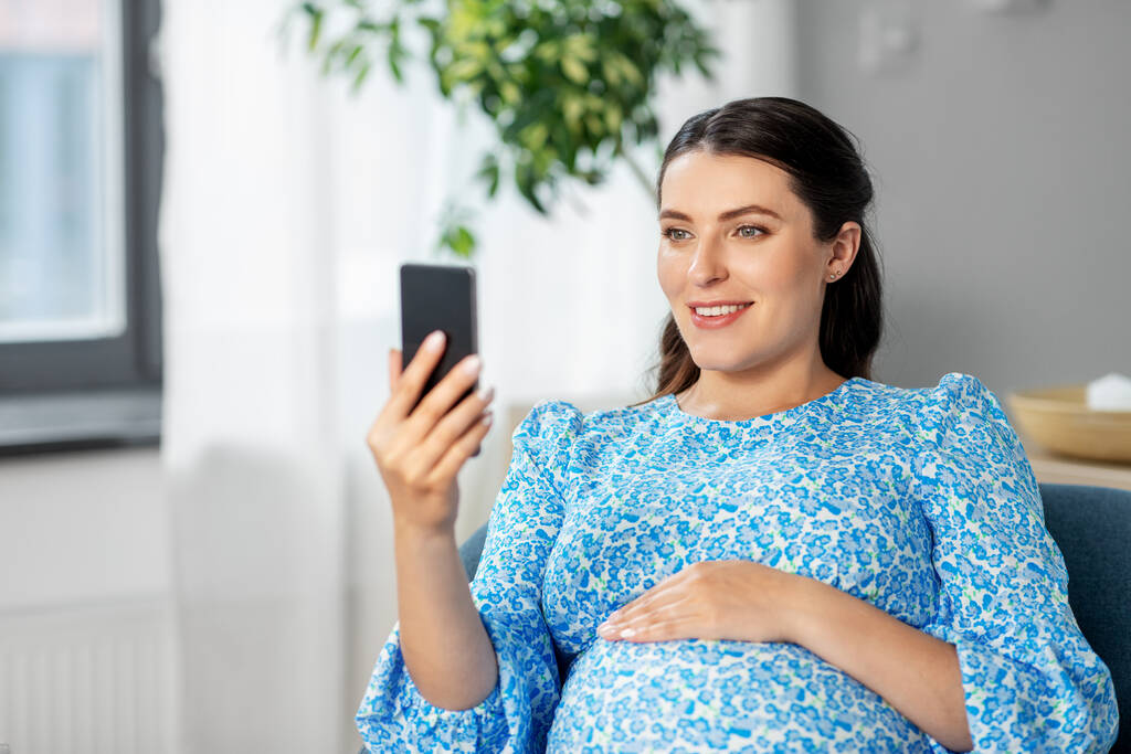 boldog terhes nő okostelefonnal otthon - Fotó, kép