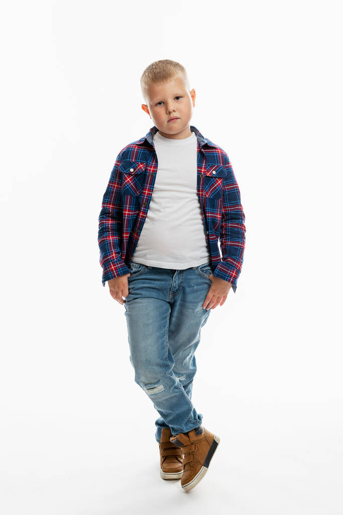 The boy is standing. A cute fat schoolboy in jeans, a shirt and a white T-shirt. Full height. White background. Vertical. - Photo, Image