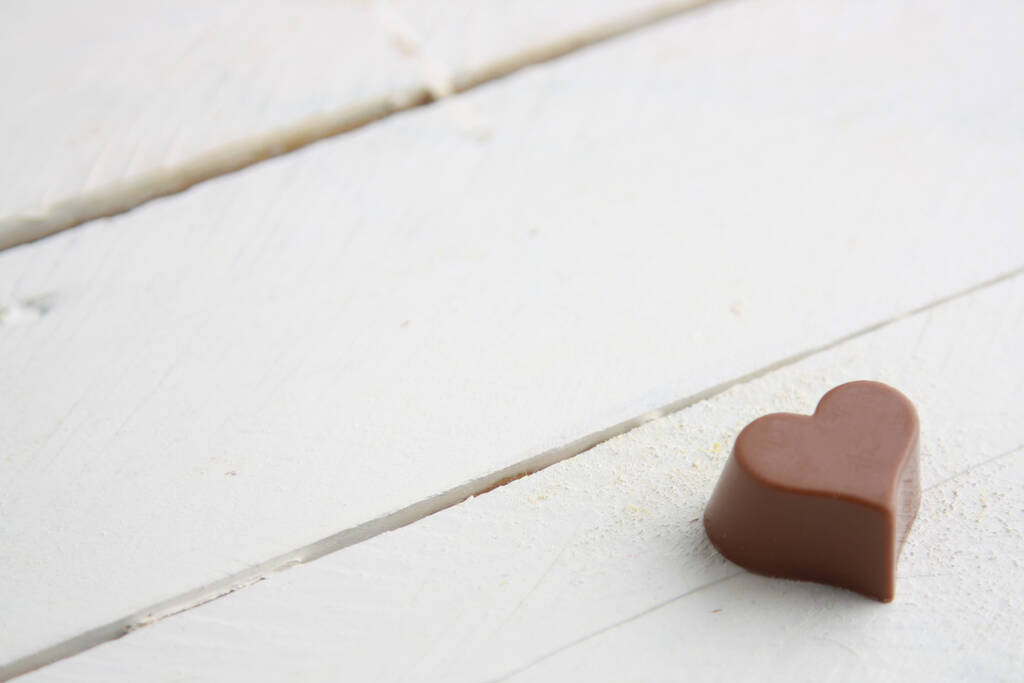 Lähikuva laukaus sydämen muotoinen suklaa karkkia valkoinen puinen pöytä - Valokuva, kuva