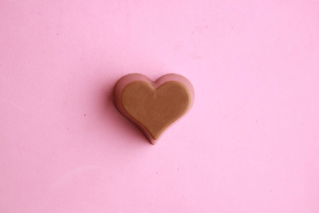 Een close-up van hartvormige chocolade op een roze oppervlak - Foto, afbeelding
