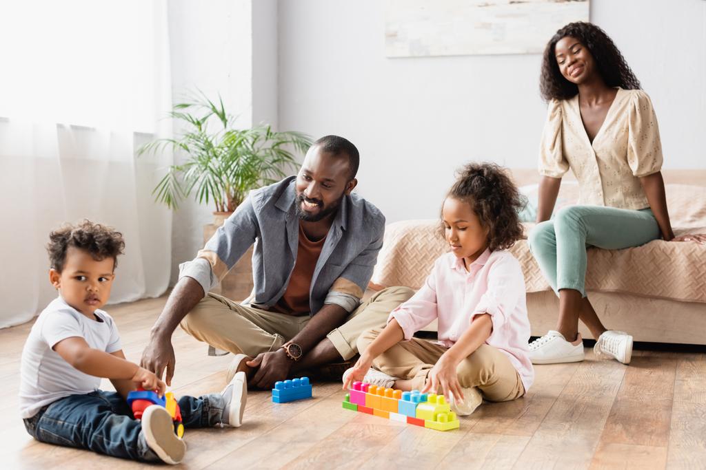 Afro-Amerikalı adam ve çocuklar, karısına yakın bir yerde oturmuş, yerde oynuyorlar. - Fotoğraf, Görsel