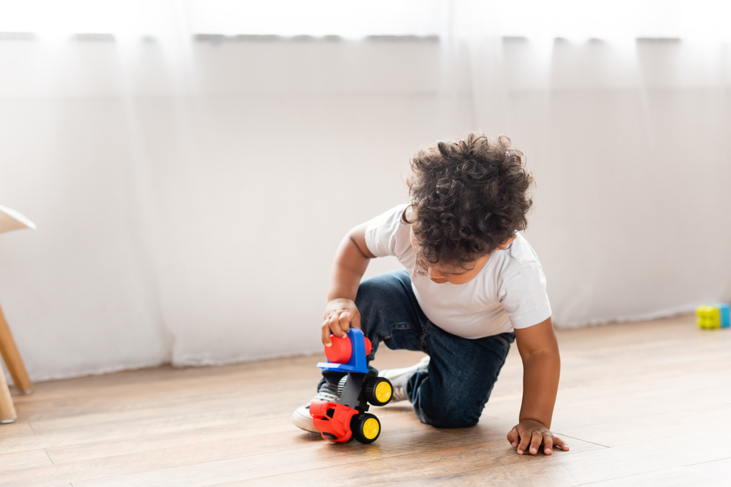 kręcone afrykański chłopiec grać z zabawka ciężarówka na drewnianej podłodze w domu - Zdjęcie, obraz