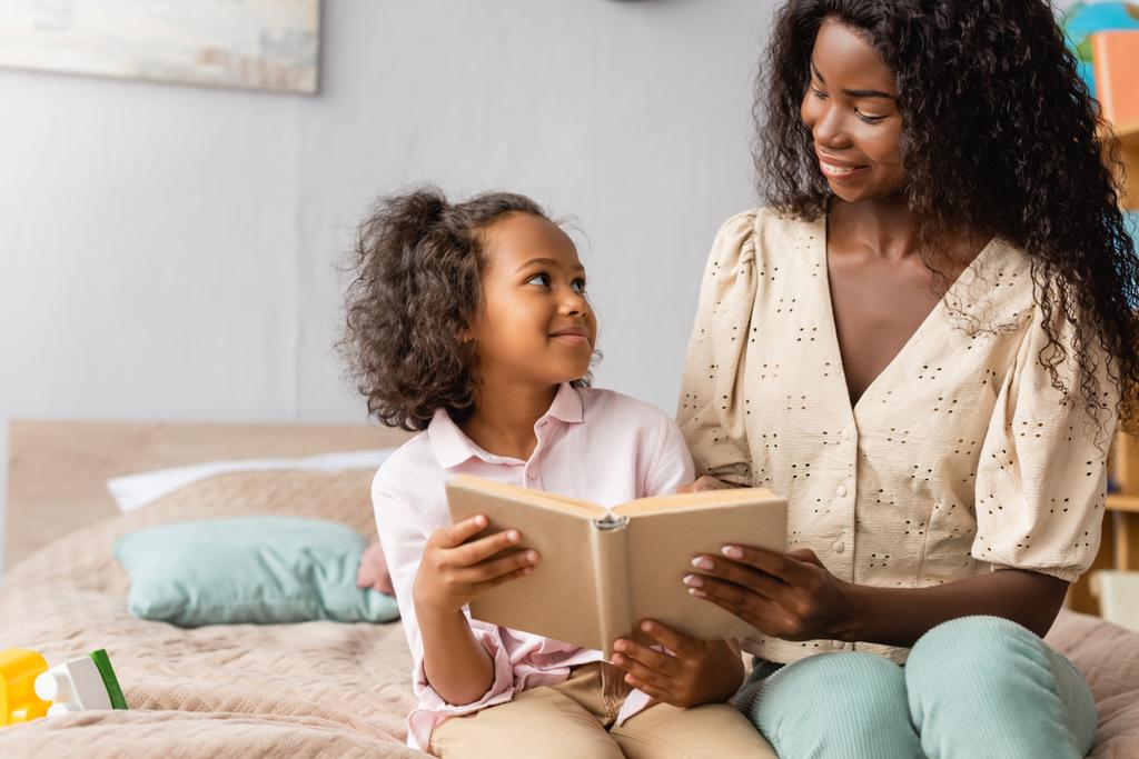 Αφροαμερικανή μητέρα και παιδί κοιτάζονται ενώ διαβάζουν μαζί το βιβλίο. - Φωτογραφία, εικόνα