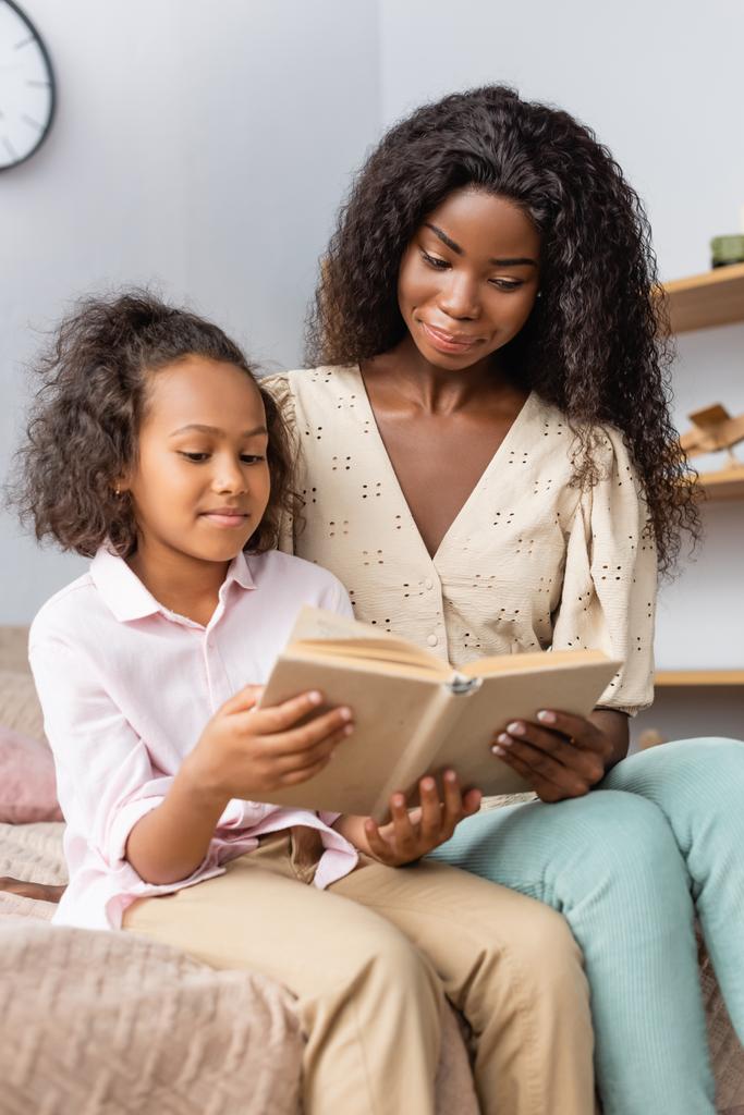 Afrykańskie amerykańskie dziecko czyta książkę siedząc obok matki w domu - Zdjęcie, obraz