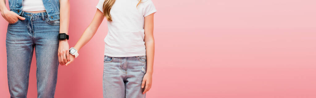 cropped view of mother and child in jeans and smartwatches holding hands on pink, website header - Photo, Image