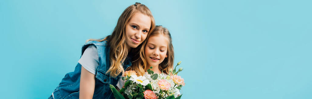 ブルーに孤立した花の花束を持つ娘の近くの若い女性のパノラマの概念 - 写真・画像