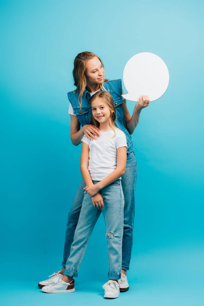 πλήρη θέα μήκος της νεαρής γυναίκας αγγίζοντας την κόρη και κρατώντας φούσκα σκέψης στο μπλε - Φωτογραφία, εικόνα