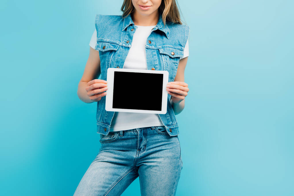 vista recortada de la mujer en ropa de mezclilla sosteniendo tableta digital con pantalla en blanco aislado en azul - Foto, Imagen
