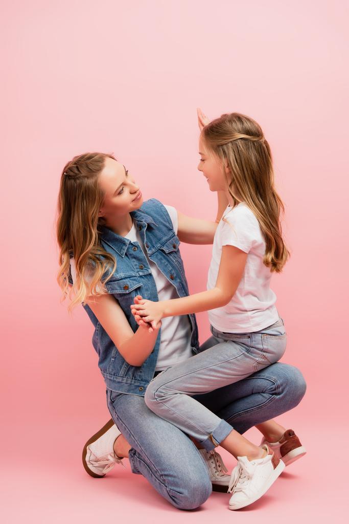 menina em t-shirt branca e jeans sentado no colo da mãe em rosa - Foto, Imagem