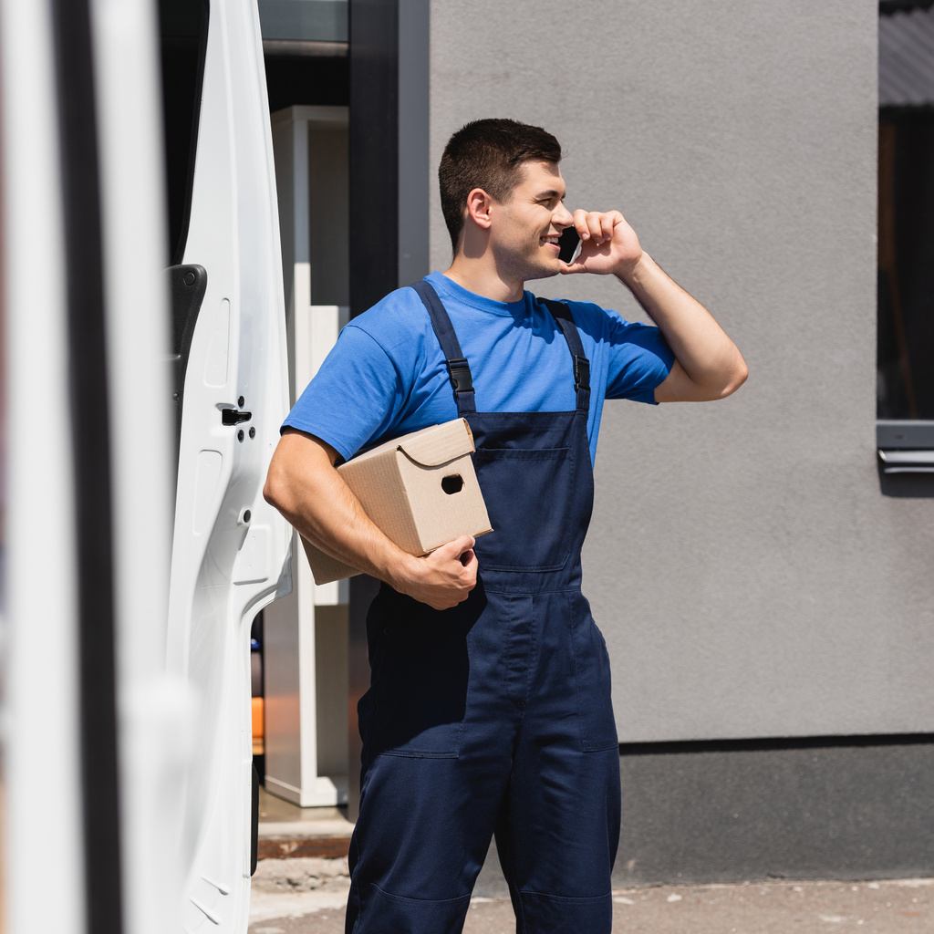 Valikoiva painopiste kuormaaja puhuu älypuhelimeen ja pitämällä pahvilaatikko lähellä kuorma kaupunkien kadulla  - Valokuva, kuva