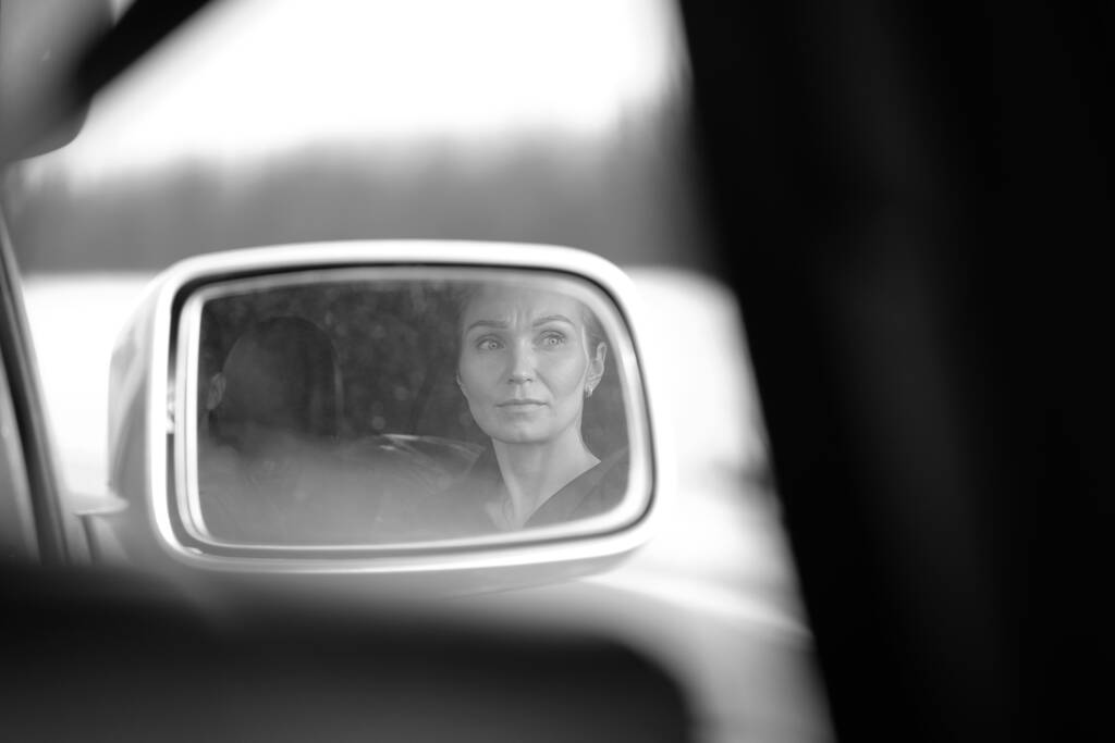 車のバックミラーで若い女性の顔と目の反射。車の女だ。白黒の画像。選択的焦点. - 写真・画像