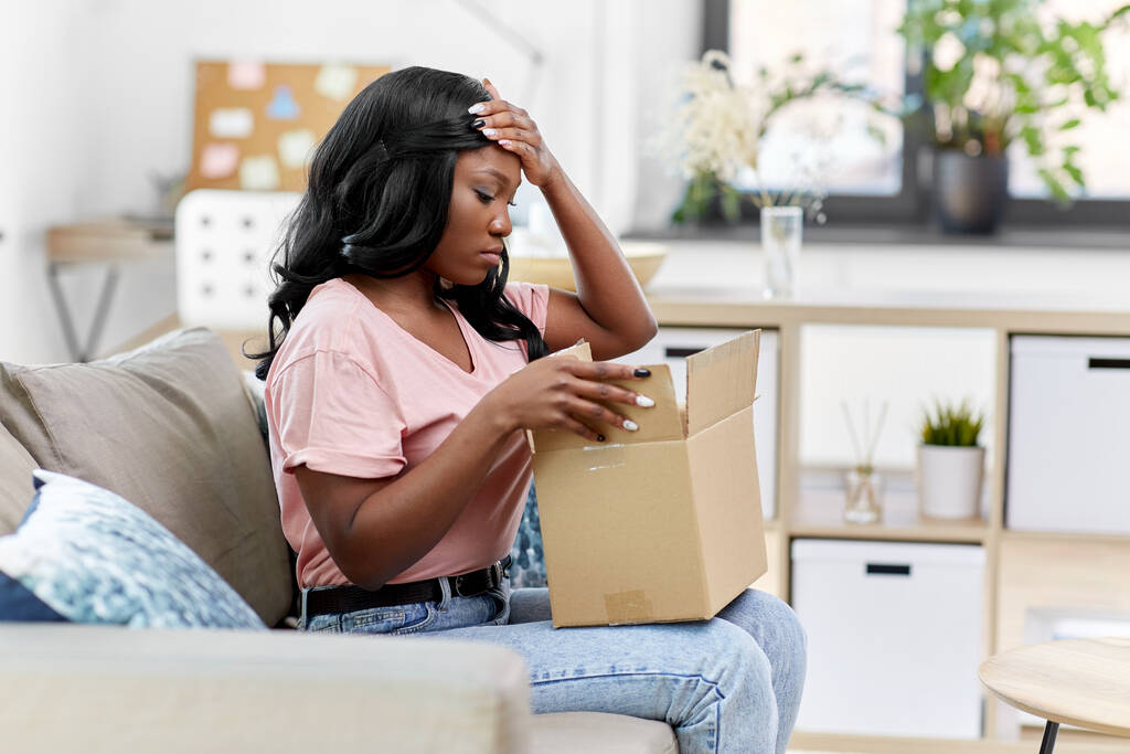 mujer afro-americana triste con caja de paquetes en casa - Foto, imagen