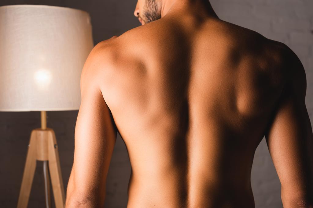 Rückenansicht eines hemdlosen Mannes, der zu Hause steht  - Foto, Bild