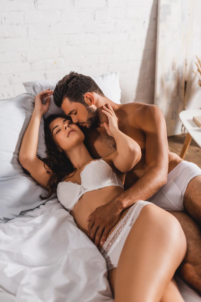 Hemdloser Mann küsst und berührt sinnliche Freundin auf Bett  - Foto, Bild