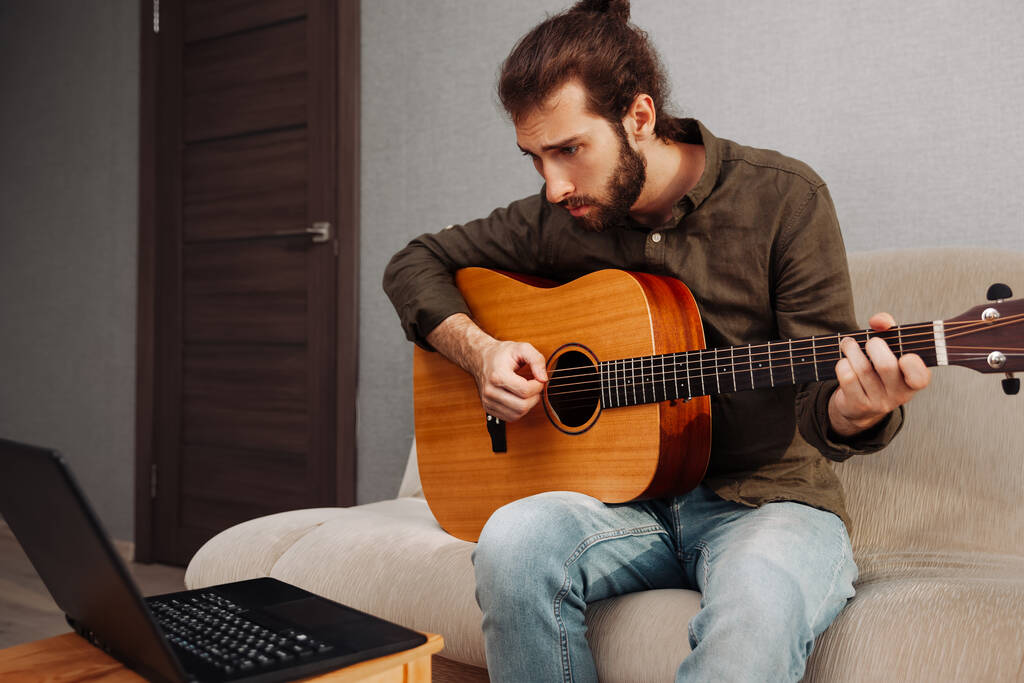 Soustředěný muž učí hrát na akustickou kytaru doma pomocí video tutorial - Fotografie, Obrázek
