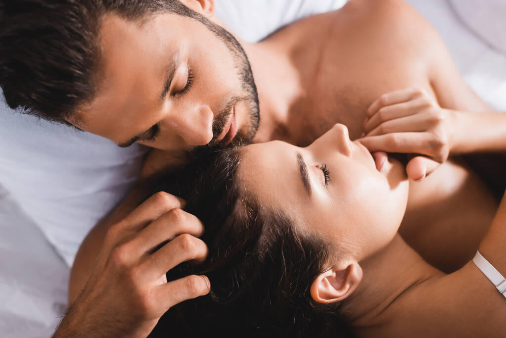Top näkymä parrakas mies koskettaa hiukset brunette nainen sängyssä  - Valokuva, kuva