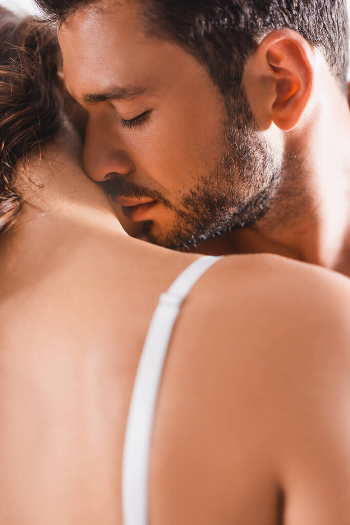 Selective focus of young bearded man kissing neck of girlfriend in bra  - Photo, Image