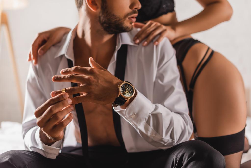 Ausgeschnittene Ansicht eines Mannes im Hemd, der seinen Ehering neben einer sinnlichen Frau auf dem Bett ablegt  - Foto, Bild