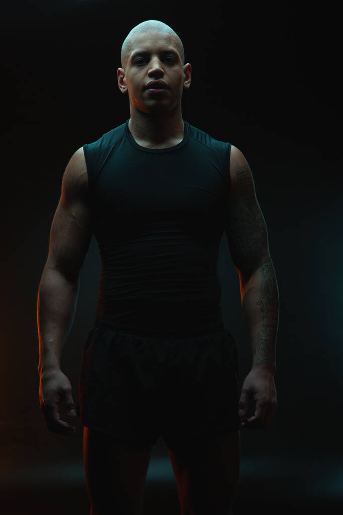 Atraktivní svalnatý potetovaný sportovec stojící osamoceně na černém pozadí - Fotografie, Obrázek