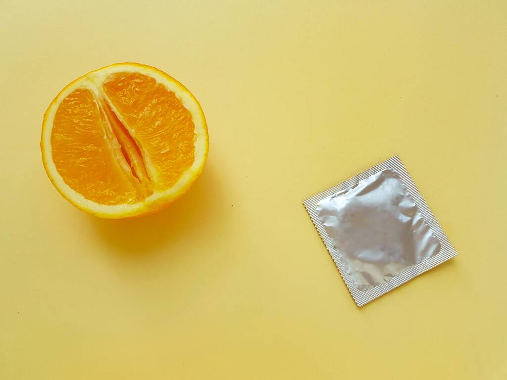 The concept of safe sex and protection. A vagina symbol. A juicy orange and a condom on a bright yellow background. - Fotó, kép