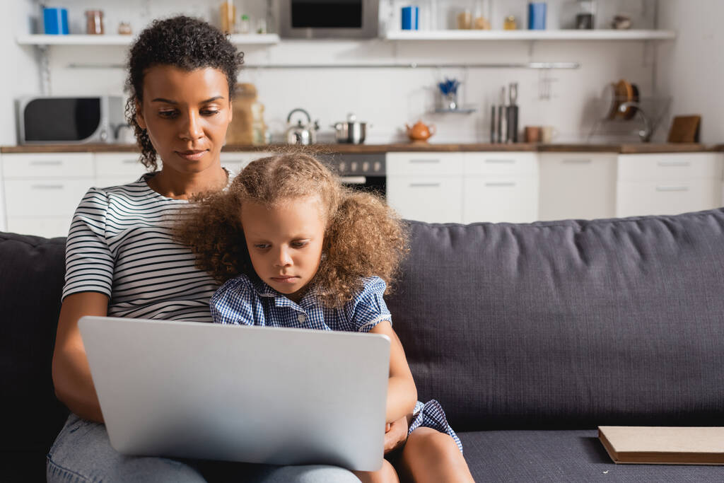 young african american freelancer using laptop while sitting on sofa with daughter - Photo, Image