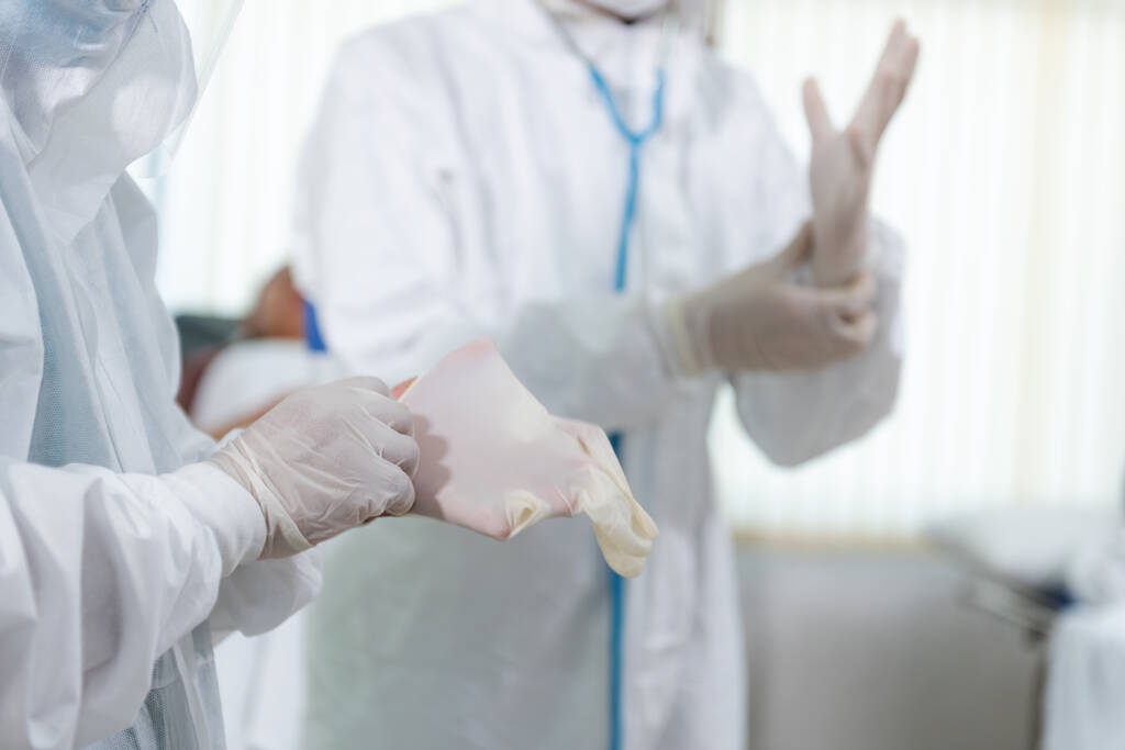 Лікарі одягають захисні рукавички та маску для костюмів перед лікуванням пацієнта в зоні контролю. Ковід-19 і коронавірусна хвороба. - Фото, зображення