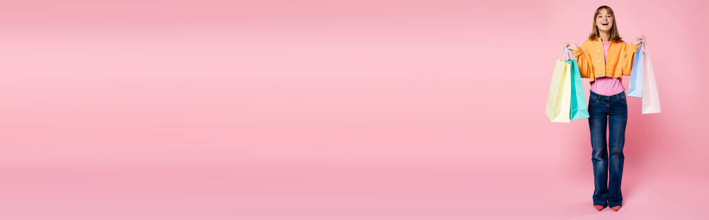 ピンクを背景にカラフルなショッピングバッグを持つ若い女性のパノラマの概念 - 写真・画像