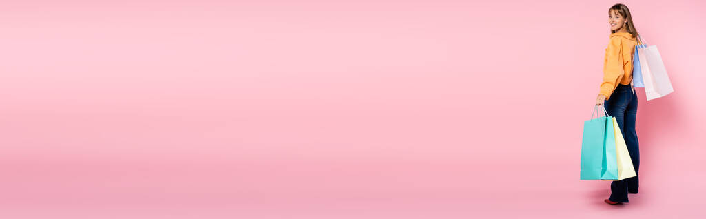 Imagen horizontal de la mujer con bolsas de compras mirando a la cámara sobre fondo rosa con espacio de copia - Foto, Imagen