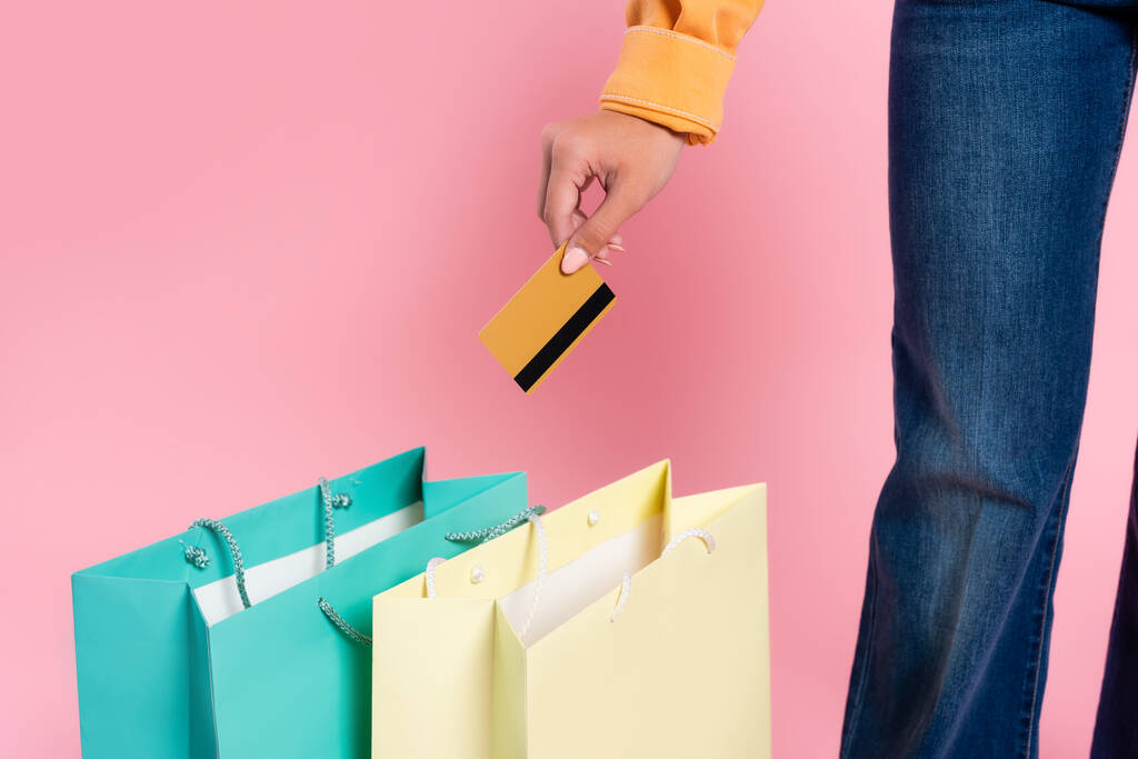 Vista recortada de la mujer que sostiene la tarjeta de crédito cerca de bolsas de compras sobre fondo rosa - Foto, imagen