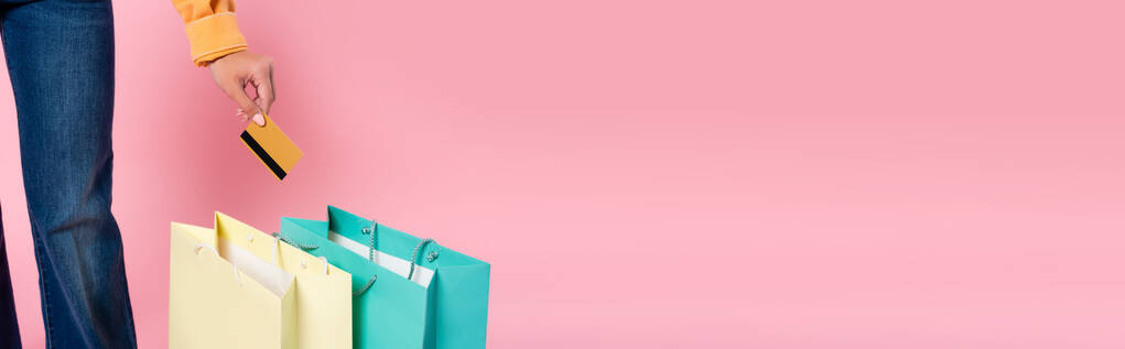 Imagem horizontal da mulher segurando cartão de crédito perto de compras em fundo rosa - Foto, Imagem