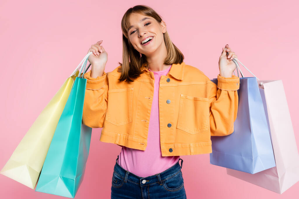 Sarı ceketli genç bir kadın pembe arka planda renkli alışverişler yapıyor. - Fotoğraf, Görsel