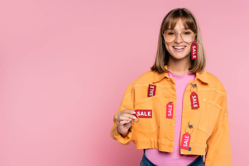 Mujer joven mostrando etiqueta de precio con letras de venta sobre fondo rosa - Foto, Imagen