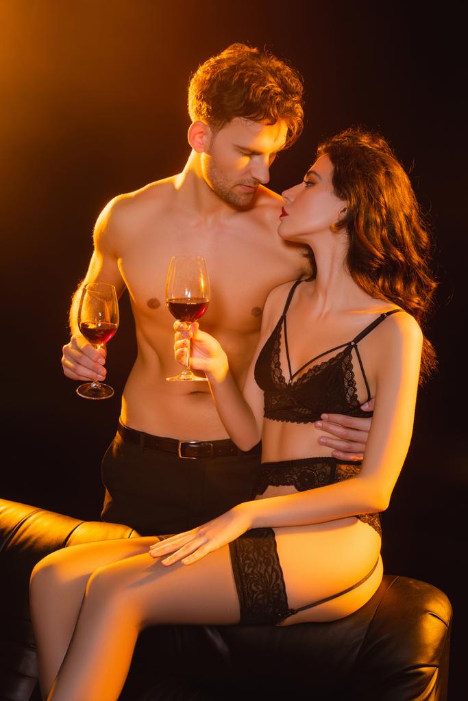 gespierde man en verleidelijke vrouw met een bril van rode wijn terwijl kijken naar elkaar op zwart  - Foto, afbeelding